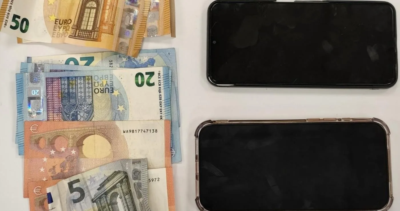 Ευρωπαϊκά χαρτονομίσματα των 5, 10, 20, 50 και 100 ευρώ τοποθετούνται πάνω σε ένα ξύλινο τραπέζι δίπλα σε τρία σπασμένα κινητά τηλέφωνα, ως μέρος των τηλεφωνικών απάτων στα Γρεβενά.
