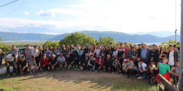 Μια μεγάλη ομάδα μαθητών από την Ελλάδα, τη Βόρεια Μακεδονία και την Αλβανία φωτογραφίζονται χαμογελαστοί με φόντο την λίμνη των Πρεσπών, συμμετέχοντας στους Σχολικούς Αγώνες Πρεσπών.