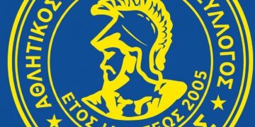 Το λογότυπο του Αία Αμυνταίου, που απεικονίζει τον Αία τον Αμυνταίο με κράνος, σε κυκλικό μπλε και κίτρινο σχέδιο, συμβολίζοντας την επιτυχημένη νίκη της ομάδας.