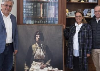 Τρεις άνθρωποι στέκονται δίπλα σε ένα μεγάλο πορτρέτο μιας γυναίκας με παραδοσιακή νυφική φορεσιά της Σιάτιστας, ως μέρος της δωρεάς ιδρύματος παπαγεωργίου στον Δήμο Βοΐου.