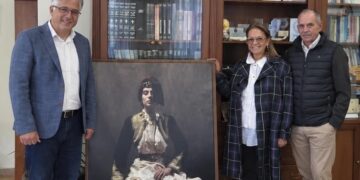 Τρεις άνθρωποι στέκονται δίπλα σε ένα μεγάλο πορτρέτο μιας γυναίκας με παραδοσιακή νυφική φορεσιά της Σιάτιστας, ως μέρος της δωρεάς ιδρύματος παπαγεωργίου στον Δήμο Βοΐου.