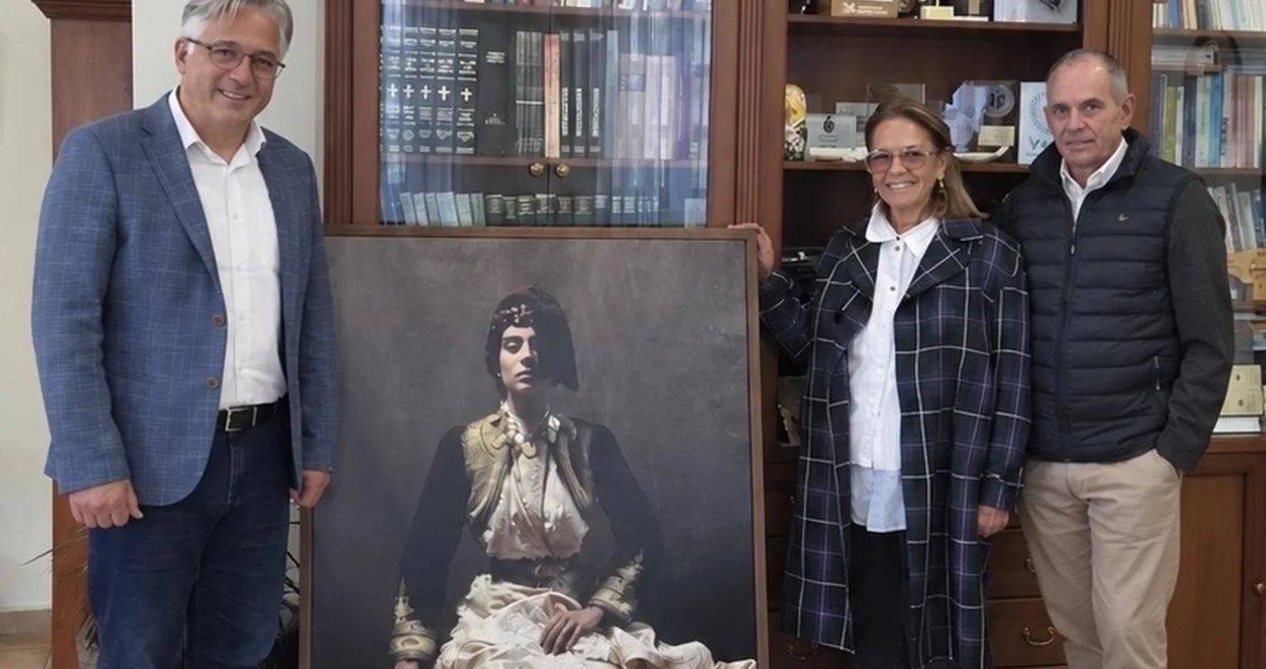 Τρεις άνθρωποι στέκονται δίπλα σε ένα μεγάλο πορτρέτο μιας γυναίκας με παραδοσιακή νυφική φορεσιά της Σιάτιστας, ως μέρος της δωρεάς ιδρύματος παπαγεωργίου στον Δήμο Βοΐου.