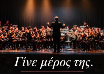 Μια ορχήστρα της Φιλαρμονικής Κοζάνης ερμηνεύει μουσική σε μια σκηνή, ενώ νέα μέλη εγγράφονται για να γίνουν μέρος της ορχήστρας Φιλαρμονική Κοζάνης.